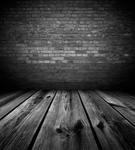 Photo of a dark and empty room, old wooden planks on the floor, old, dark brick wall blocks the way out.